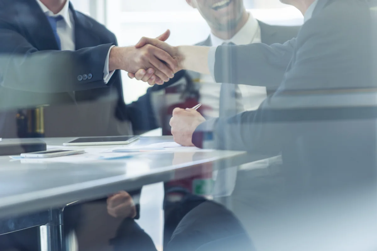 Business partners shaking hands across a boardroom table