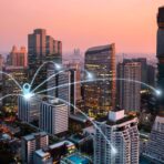 Downtown office towers at dusk, linked by glowing network lines across the city skyline