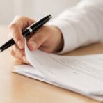 Person turning the pages of a printed business contract while holding a pen at a desk