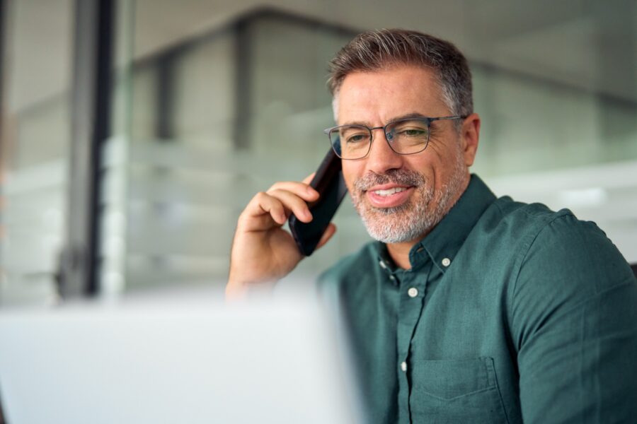 Business executive taking a phone call at his desk with an open laptop in front of him